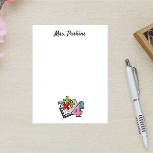May include: A white notepad with the text "Mrs. Parkins" at the top. The notepad has a colorful illustration of a book with math symbols on it.