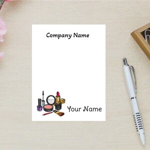 May include: A white notepad with the text "Company Name" and "Your Name" printed on it. The notepad has a small illustration of makeup products, including lipstick, nail polish, and a makeup brush.