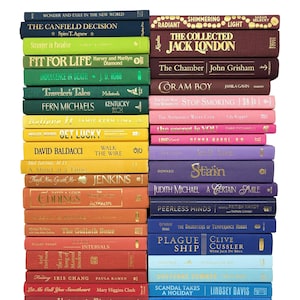 May include: A collection of hardcover books with colorful spines, arranged in two vertical stacks. The books feature titles and author names in various fonts and colors, creating a visually appealing display. The books are of different sizes and colors.