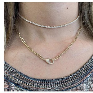 May include: Two gold necklaces with diamond accents. The top necklace is a thin, delicate chain with small diamonds. The bottom necklace is a thicker chain with a larger, diamond-encrusted clasp.