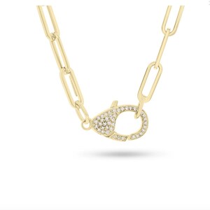 May include: A gold chain necklace with a pave diamond clasp. The chain is made of linked ovals.