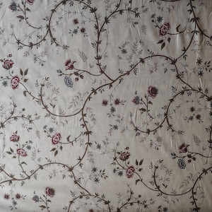 Puede incluir: Tela color crema con un patrón floral repetido. Enredaderas marrón oscuro con hojas pequeñas y racimos de flores rojas y azules crean un diseño delicado y vintage. La tela tiene una textura ligeramente arrugada.