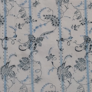 Op de afbeelding: Een witte stof met een herhalend patroon van blauwe en zwarte gestileerde bloemenontwerpen. Het patroon omvat delicate ranken, bladeren en bloemen.