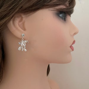 May include: Silver-toned dangle earrings with a floral design. The earrings feature clear crystals and small, white pearls. The earrings are attached to a small, round crystal stud.