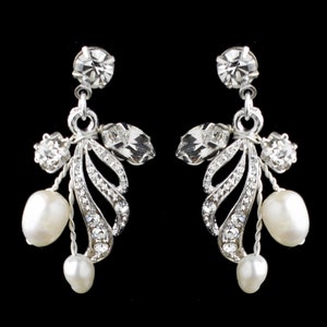 May include: Elegant silver-toned drop earrings with a floral design. Each earring features a large, round clear crystal at the top, with smaller crystals and a leaf-like design. Two white, teardrop-shaped pearls dangle from each earring. The background is black.