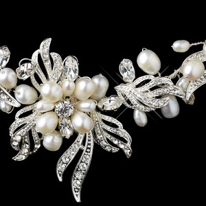 May include: A silver-toned bridal hair accessory featuring clusters of white pearls and clear crystals. The design incorporates stylized leaf shapes, with the crystals adding sparkle. The background is black, highlighting the details of the piece.