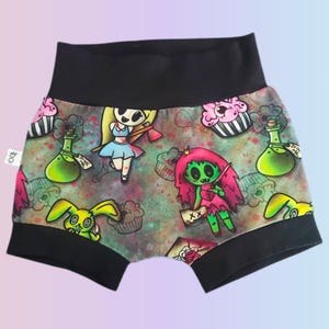 May include: Black and patterned underwear featuring cartoon characters, cupcakes, and potion bottles. The design includes a green zombie with pink hair, a blonde girl with an axe, and a yellow rabbit. The waistband and leg openings are black.