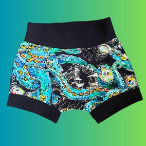 May include: Black and teal octopus-themed shorts with a high waistband. The shorts feature a repeating pattern of octopus tentacles and eyes in teal, yellow, and blue against a black background. The waistband and leg openings are solid black.