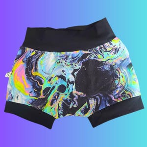 May include: Black and colorful patterned shorts. The shorts feature a high waistband and leg openings in solid black. The fabric has a swirling, abstract design with shades of blue, green, yellow, and pink against a black background.