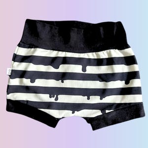 May include: Black and white striped baby shorts with a unique dripping design. The shorts have a black waistband and leg openings. The fabric is a soft material, perfect for comfort and style.