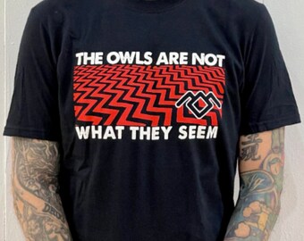 May include: Black t-shirt with a red and black chevron pattern and a white logo that says "The Owls Are Not What They Seem".
