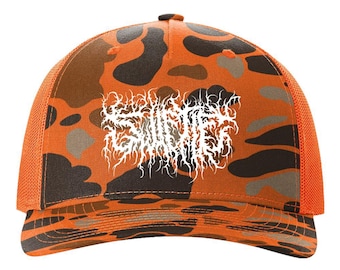 May include: A trucker hat featuring an orange, brown, and black camouflage pattern on the front panels and brim. The back panels are made of orange mesh. Centered on the front is a white graphic design with intricate, jagged, vine-like lettering.