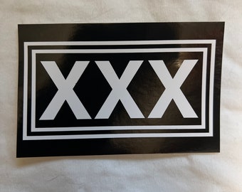 May include: Black and white sticker with the word "XXX" in a bold, white font inside a black double-lined rectangle.