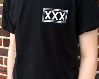 May include: Black t-shirt with a white box containing the text "XXX" printed on the front.