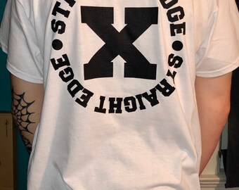 May include: White t-shirt with a black circle graphic on the back. The circle graphic has a black X in the center and the text "STRAIGHT EDGE" written around the outside of the circle.