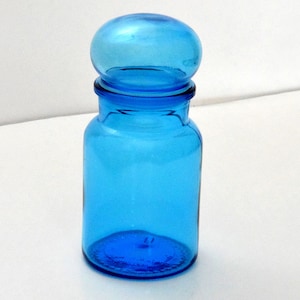 May include: A bright blue glass jar with a rounded lid. The jar is clear and has a smooth surface.