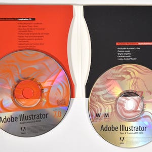 May include: Two CD-ROMs for Adobe Illustrator 7.0. The application CD-ROM is red and orange with the text "Adobe Illustrator 7.0 Application CD-ROM". The tour and training CD-ROM is gold and red with the text "Adobe Illustrator 7.0 Tour & Training CD-ROM".