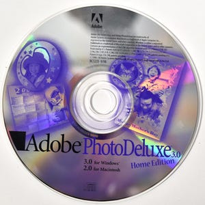 May include: A silver Adobe PhotoDeluxe 3.0 CD-ROM for Windows and Macintosh. The disc features a holographic design with images of people and the text "Happy Mother's Day". The disc also has the Adobe logo.