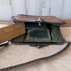 May include: Vintage brown leather purse with a metal clasp and chain strap. The purse is open, revealing a green interior and a small mirror. A wooden ruler is placed next to the purse, showing measurements in inches.