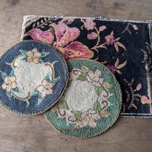 May include: Three vintage textile items: two round coasters and a rectangular mat. The coasters feature floral designs in blue, green, and cream, with gold trim. The mat has a black background with pink and orange floral patterns.