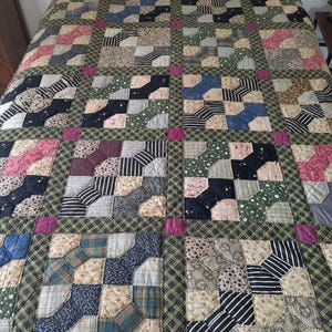 May include: A patchwork quilt with a repeating pattern of squares and diamonds in shades of pink, green, blue, and black.