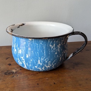 May include: A blue and white enamelware bowl with a black rim and handle. The bowl has a mottled, marbled pattern.