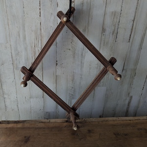 May include: An expandable wooden wall rack featuring a diamond-shaped lattice design with multiple pegs. The rack is constructed from dark brown wood with vertical grooved detailing and small, light-colored rounded tips on each peg end.