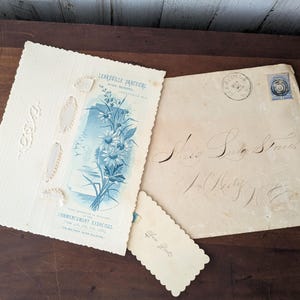 May include: A collection of vintage ephemera, including a cream-coloured commencement program with blue floral illustrations and the text "LEAKSVILLE PRACTICAL HIGH SCHOOL". An aged envelope with cursive script and a postage stamp.