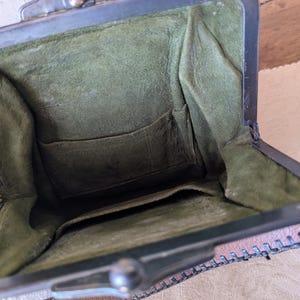 May include: Open view of a vintage brown leather purse with a metal clasp. The interior is lined with olive green fabric and features a small pocket. The purse is open, revealing its contents.