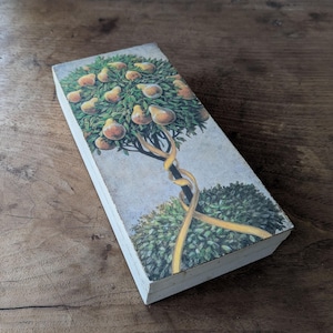 May include: Rectangular box with a painted illustration of a pear tree with ripe pears. The tree has a yellow ribbon wrapped around the trunk and branches. The box is set on a wooden surface.