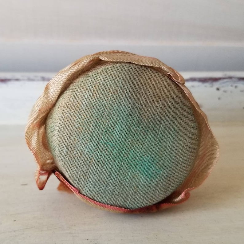 May include: A round, cream-colored pincushion with a green fabric center and a ruffled edge.