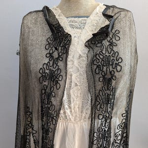 May include: A black lace shawl with a delicate floral pattern. The shawl is sheer and has a scalloped edge.