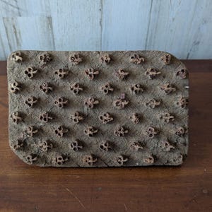 Puede incluir: Un bloque de impresión rectangular de madera con un patrón floral repetitivo. El bloque es de color marrón desgastado, con el diseño floral en un tono más oscuro y texturizado. Los bordes son ligeramente redondeados.
