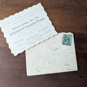 May include: An old invitation and envelope on a wooden surface. The invitation has a torn edge and text that reads "Altoona Lodge, No. 287, Brotherhood of Locomotive Firemen." The envelope has a green stamp and handwritten address.