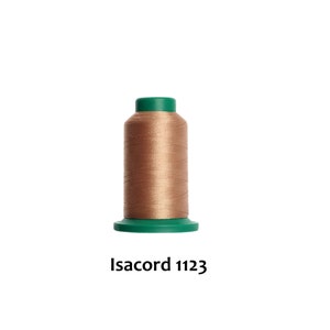 May include: A spool of brown thread with a green plastic top and bottom. The text "Isacord 1123" is printed below the spool.