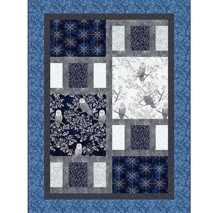 May include: A quilted patchwork blanket with a blue border and a rectangular pattern. The pattern features squares of dark blue floral, white, and gray fabrics. Owls perch on branches in some squares. A decorative home textile.