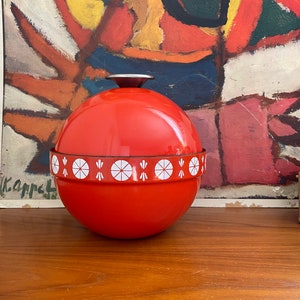 May include: A red and white enamelware bowl with a white geometric design. The bowl is round and has a lid.