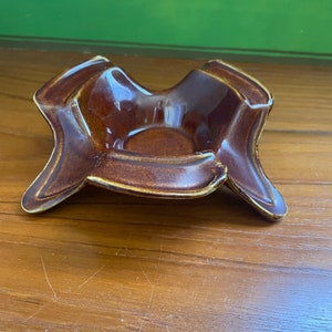 May include: A brown ceramic ashtray with a four-pointed star shape.