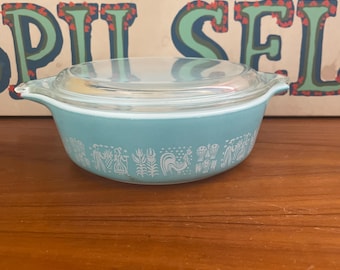May include: A light blue casserole dish with a clear glass lid. The dish features a white design of people, flowers, and a rooster.
