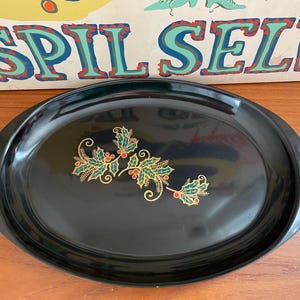 May include: Black oval serving tray with a glossy finish. The tray is decorated with a gold, green, and red holly design. The word "SPIL SELV" is visible in the background.