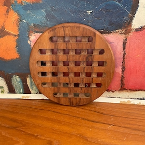 May include: A round wooden coaster with a woven pattern. The coaster is made of dark brown wood and has a natural finish.
