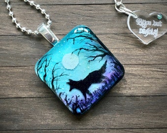 May include: A silver chain necklace with a square glass pendant featuring a blue and purple watercolor painting of a wolf silhouetted against a moonlit forest. The pendant is attached to a silver bail. The necklace also includes a separate silver chain with a clear heart-shaped pendant that says "You are but a dragonfly".