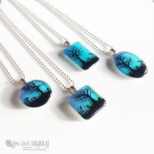 May include: Four silver necklaces with blue and black resin pendants featuring a silhouette of a tree and a graveyard. The pendants are in different shapes, including round, oval, and square.
