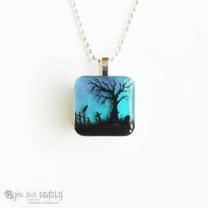 May include: A square glass pendant necklace with a black silhouette of a tree, a crow, and a tombstone against a blue and purple background.