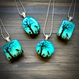 May include: Four glass pendants on silver chains, each featuring a dark silhouette of a tree with crows and a graveyard against a teal and blue gradient background.