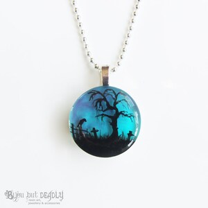May include: A silver chain necklace with a round pendant featuring a hand-painted silhouette of a tree and a fence against a blue and purple sky.