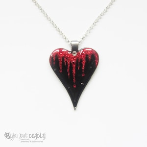 May include: A silver chain necklace with a black and red heart pendant. The heart is dripping with red glitter and has a small silver rhinestone in the center.