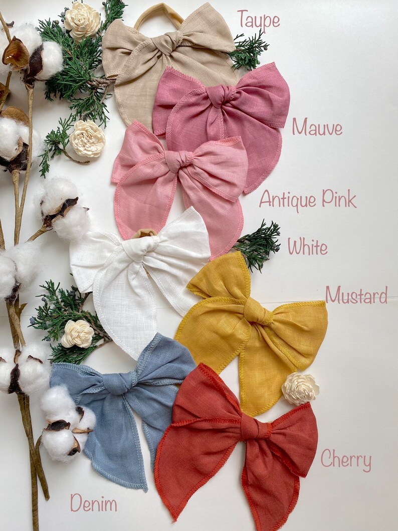 May include: Ten fabric hair bows in various colors, including taupe, mauve, antique pink, white, mustard, cherry, and denim. The bows are arranged in a circle on a white background.