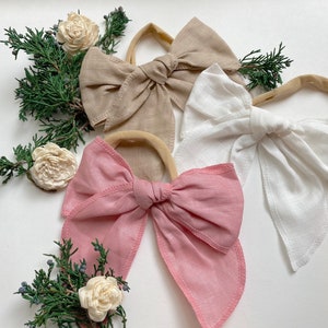 May include: Three fabric hair bows with elastic bands. The bows are in shades of pink, beige, and white.