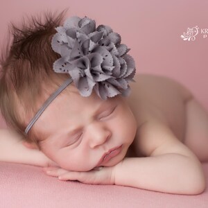 Puede incluir: Una bebé durmiendo con una diadema de flores grises sobre un fondo rosa.